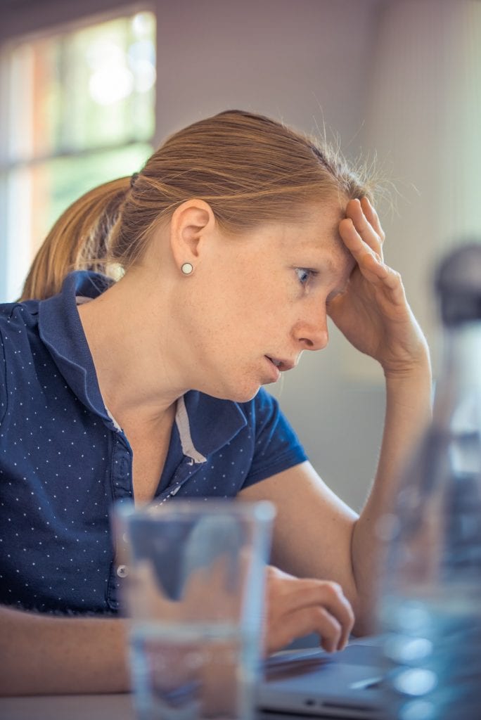 woman with head in hands at laptop frustrated with business sale regrets